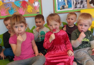 Dzieci siedzą na dywanie i jedzą lizaki w kształcie serca